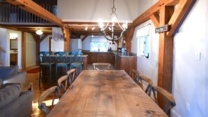 Un coin repas avec une table et des chaises en bois, un lustre et une cuisine en arrière-plan.