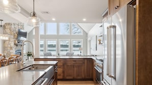 A modern kitchen with a large island, stainless steel appliances, wooden cabinets, and a stone accent wall.