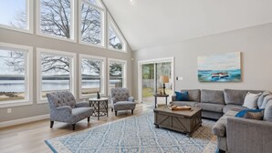 A spacious living room with large windows, a gray sofa, a coffee table, and a blue patterned rug.
