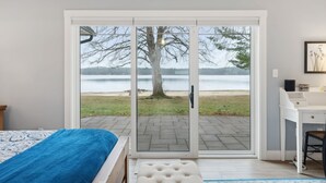 A bedroom with a large sliding glass door leading to a patio with a view of a lake and a tree.