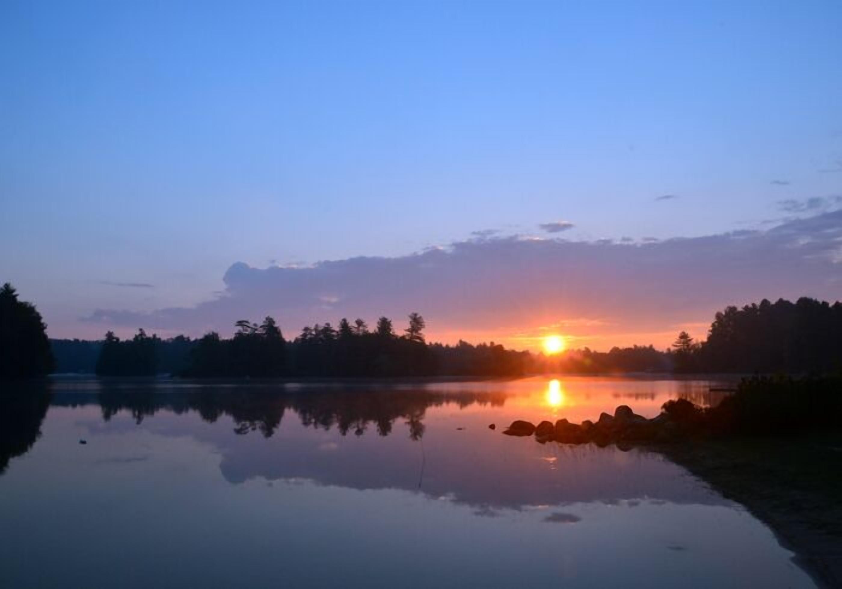 Un lago tranquilo al atardecer con árboles reflejándose en el agua.