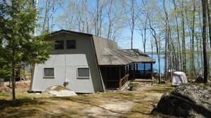 A cabin with a large deck overlooking a lake, surrounded by trees.