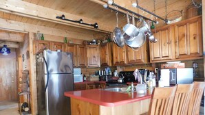 A kitchen with wooden cabinets, a stainless steel refrigerator, hanging pots, a microwave, and a wooden island with a chair.