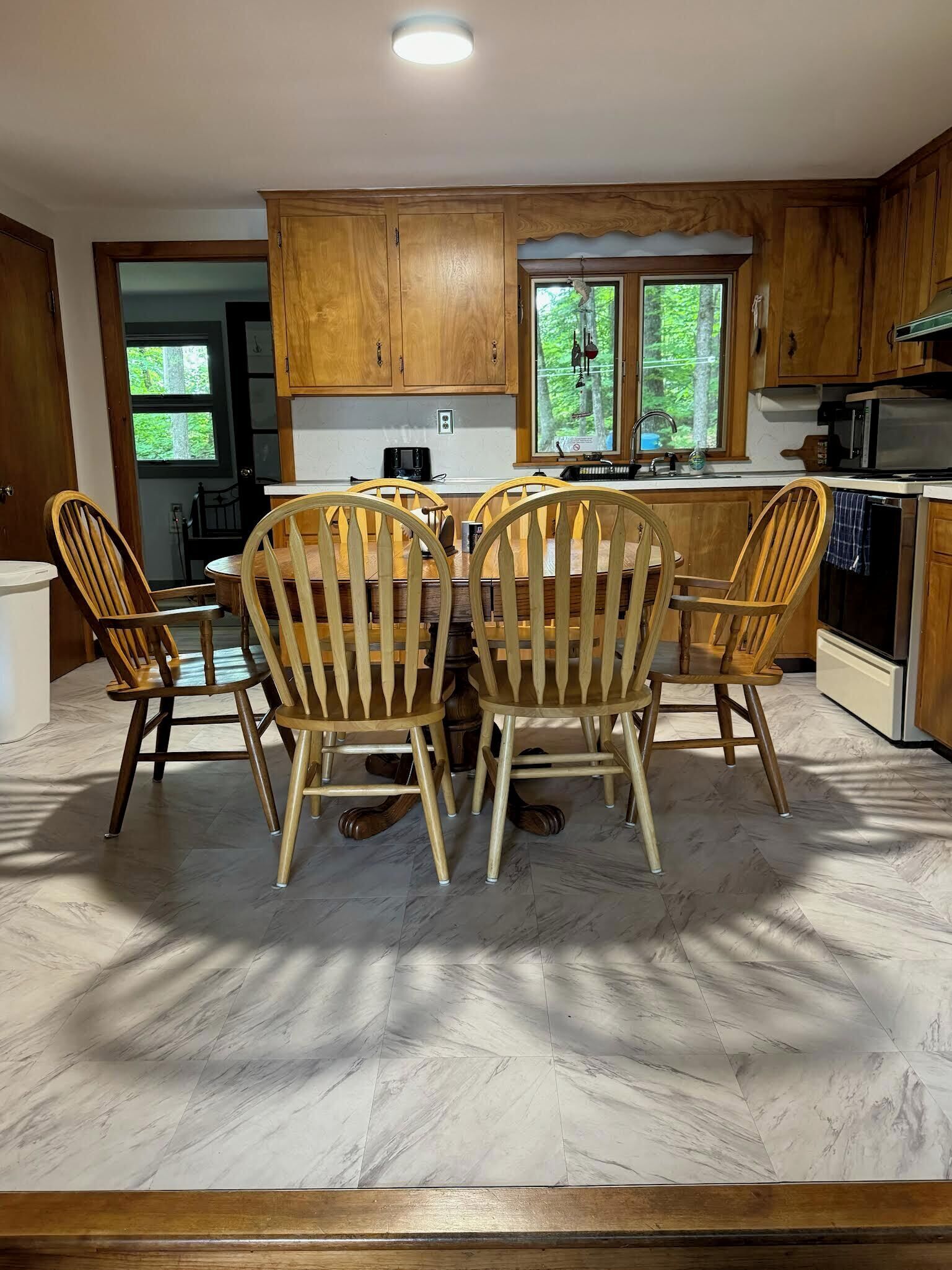 Una cocina con armarios de madera, una mesa de comedor con seis sillas y una ventana con vista a árboles.