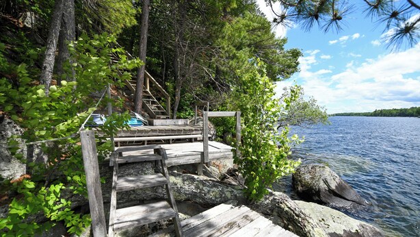A wooden dock leading to a docked boat, surrounded by trees and a calm lake. - SUMMER SPECIAL Vintage cottage w/ beautiful mountain views across Sebago Lake (Raymond)