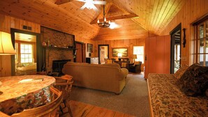 A cozy cabin interior with a fireplace, wooden walls, a sofa, and a dining table. - SUMMER SPECIAL Vintage cottage w/ beautiful mountain views across Sebago Lake (Raymond)