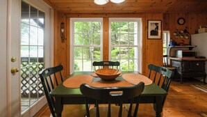 A wooden-paneled room with a dining table, chairs, a wooden bowl, and a stove. - SUMMER SPECIAL Vintage cottage w/ beautiful mountain views across Sebago Lake (Raymond)