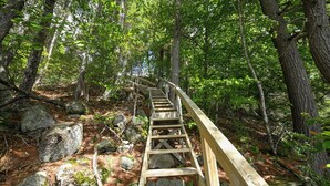 A wooden staircase in a forested area with large rocks and trees. - SUMMER SPECIAL Vintage cottage w/ beautiful mountain views across Sebago Lake (Raymond)