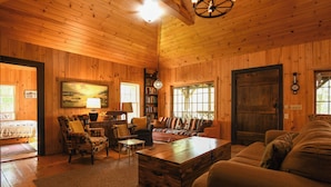 A cozy wooden cabin interior with a sofa, armchairs, a coffee table, and a bookshelf. - SUMMER SPECIAL Vintage cottage w/ beautiful mountain views across Sebago Lake (Raymond)
