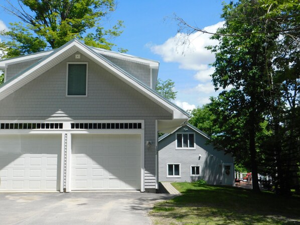 A two-story house with a garage, a small porch, and a covered outdoor area. - Beautiful home on Sebago Lake Basin with expansive yard and sandy beach! (Standish)
