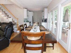 A dining area with a wooden table set for four, surrounded by chairs with woven placemats. A glass vase with a candle is on the table. - Beautiful home on Sebago Lake Basin with expansive yard and sandy beach! (Standish)
