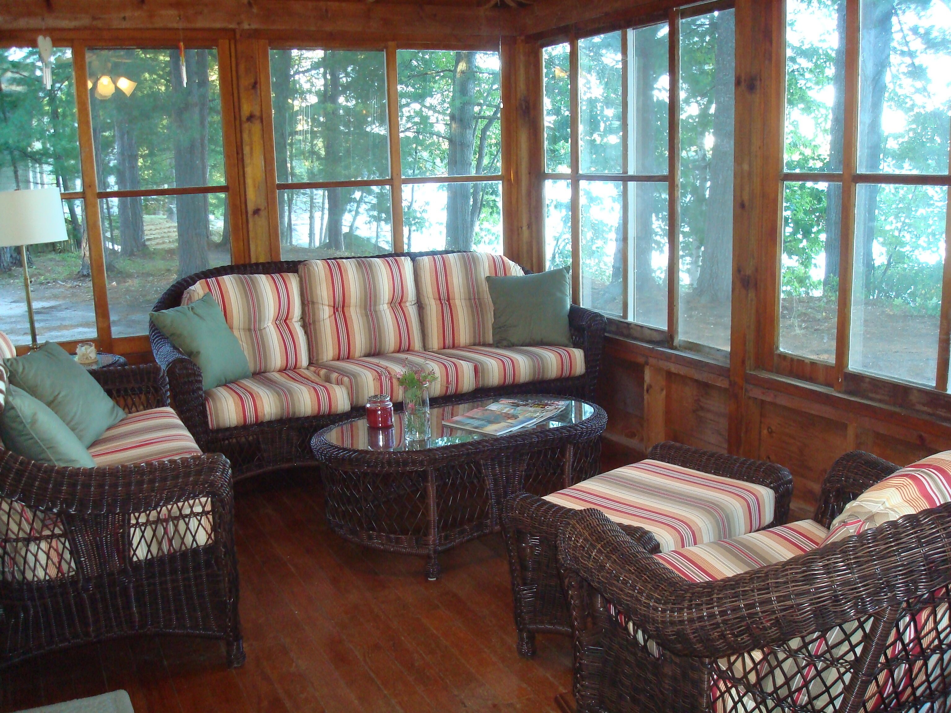 A cozy indoor seating area with wicker furniture, large windows, and a view of the forest.