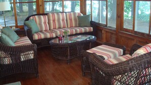 Un espace intérieur accueillant, aménagé avec des meubles en osier, de grandes fenêtres et offrant une vue sur la forêt.
