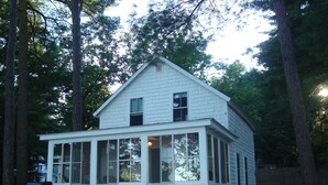 Une maison blanche à deux étages, dotée d’un porche abrité et entourée d’arbres.