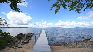 A wooden pier extending into calm water, surrounded by rocks and pebbles, with a clear sky above.