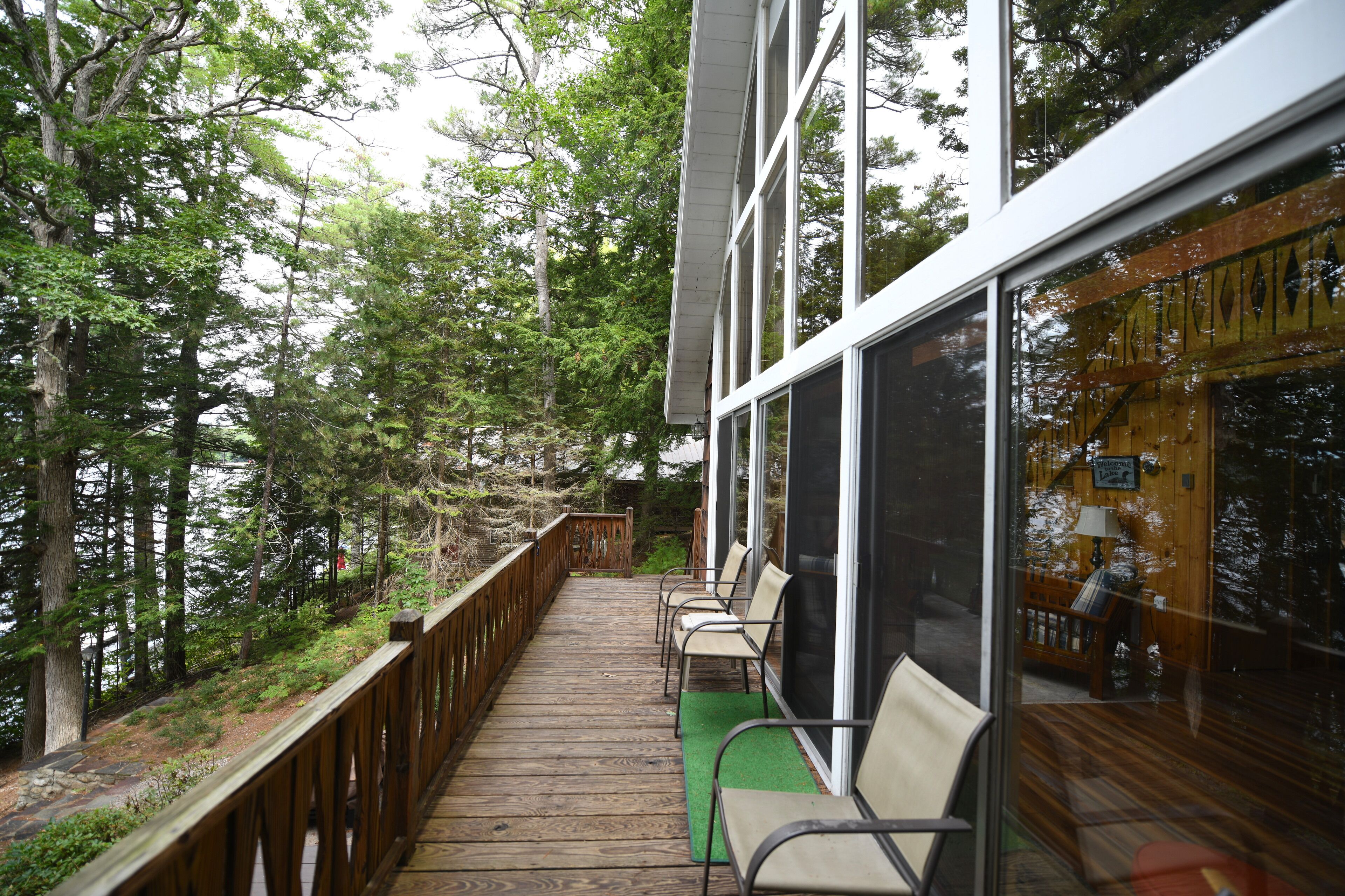 A wooden deck with chairs and a green mat, overlooking a forested area.