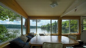 Ein Essbereich mit Holztisch und Stühlen, große Fenster mit Blick auf einen See und einen Wald.