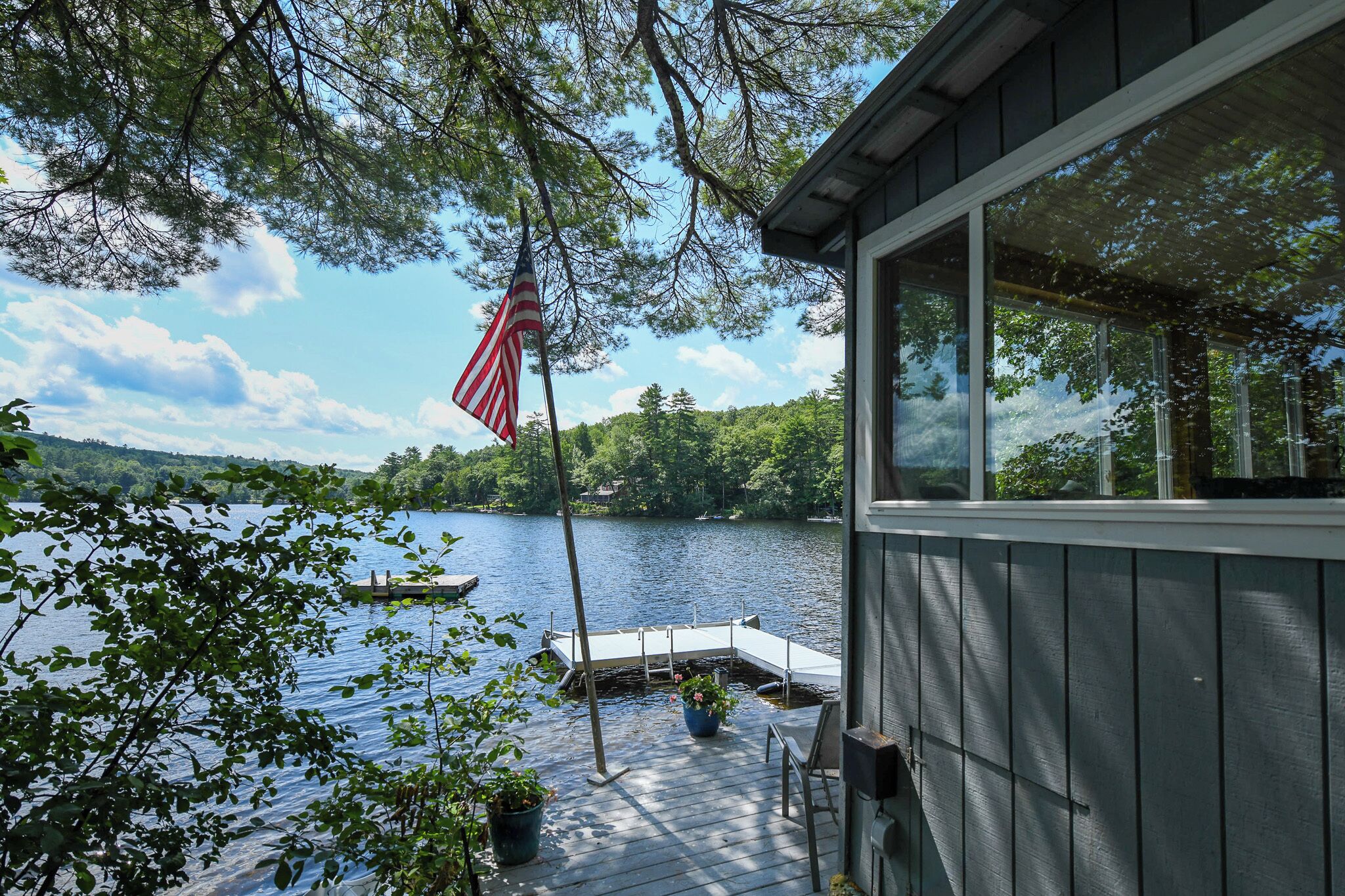 A lakeside cabin with a dock, potted plants, and an American flag.