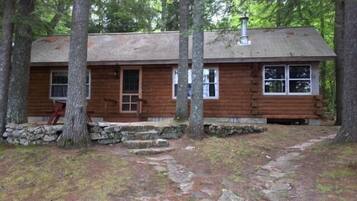 A rustic cabin with a stone foundation, wooden walls, and a chimney.