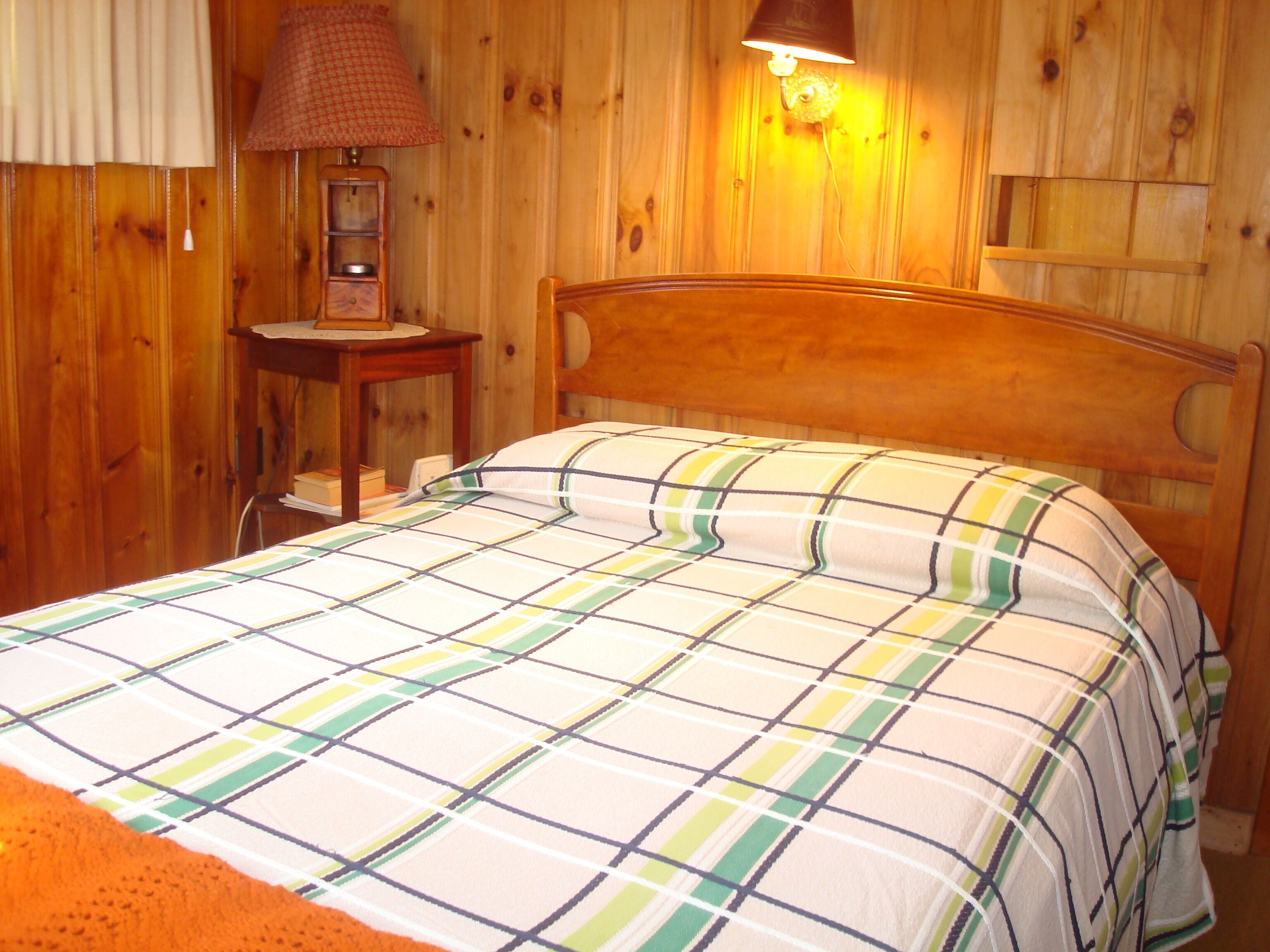 Ein Zimmer mit Holzboden, einem Bett, einem Nachttisch, einer Lampe und einem an der Wand befestigten Regal.