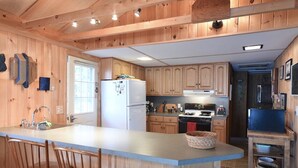 Una cocina con armarios de madera, una isla central con taburetes de bar, un refrigerador, estufa y un lavabo.