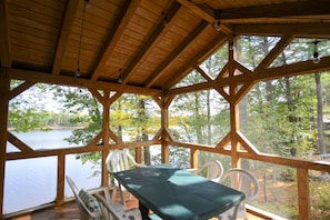 A wooden deck with a table and chairs overlooking a lake, surrounded by trees.