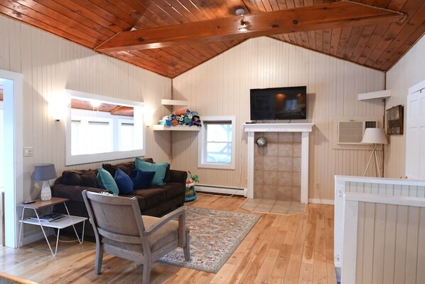 A cozy living room with a wooden ceiling, a fireplace, a television, and a sofa with cushions.