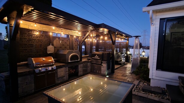 Un área de cocina al aire libre con una parrilla, horno para pizzas y una mesa de vidrio.
