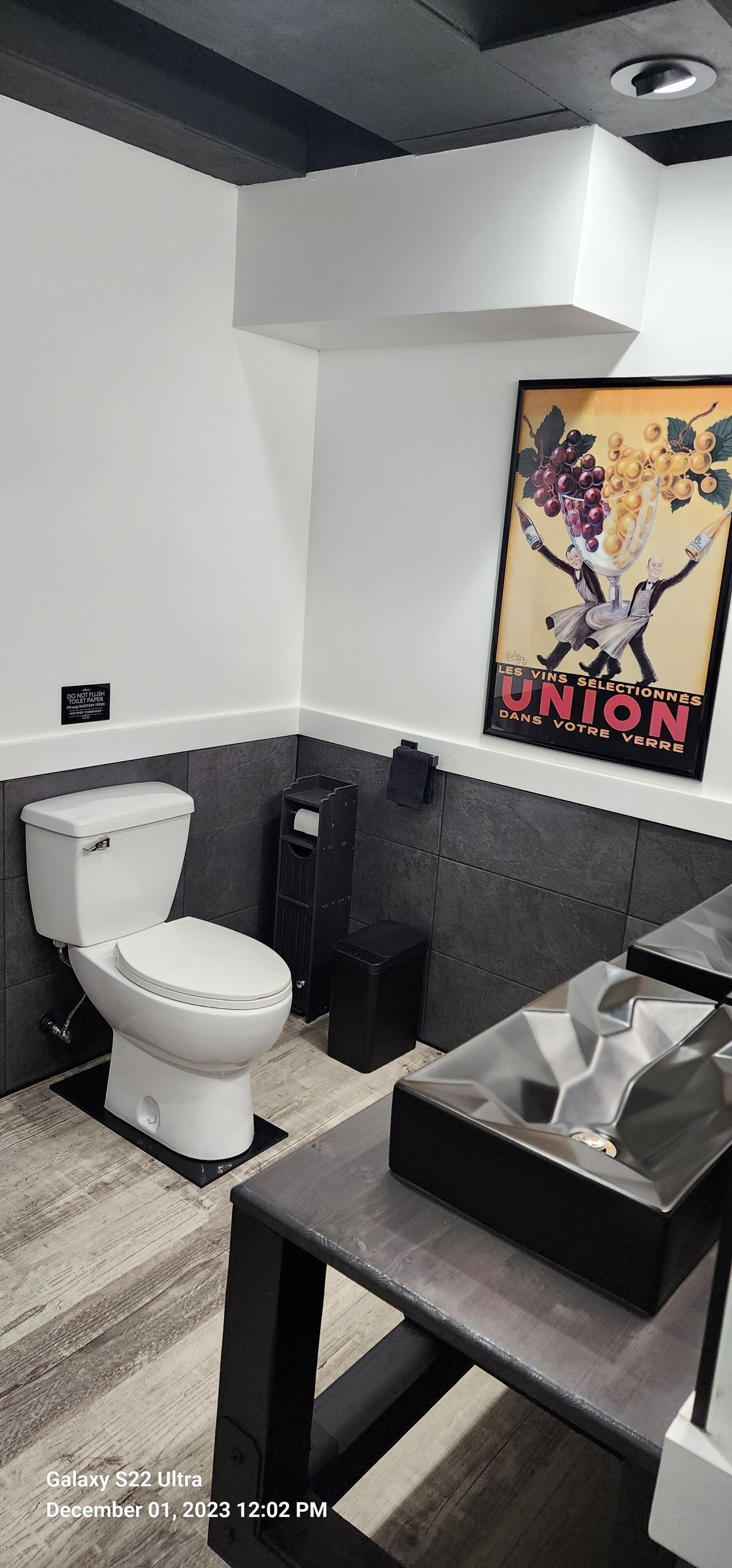 Een moderne badkamer met een wit toilet, een zwarte wastafel en een poster aan de muur.