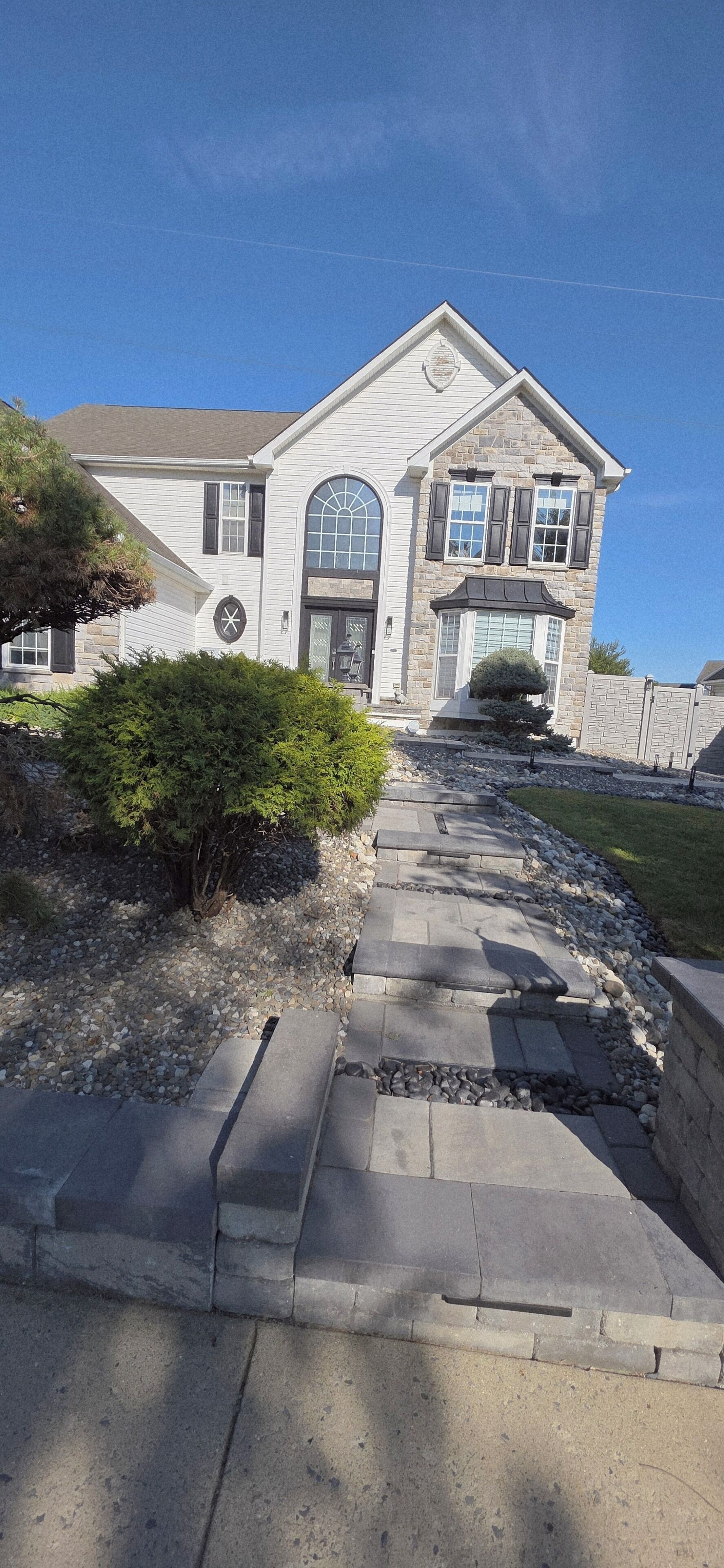 A two-story house with a stone facade, a large arched window, and a front porch.