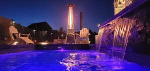 A swimming pool with a waterfall feature, surrounded by lounge chairs and a tall illuminated structure in the background. - Staycation Oasis! A unique Experience!

Heated salt water pool closing 11/01 (Easton)