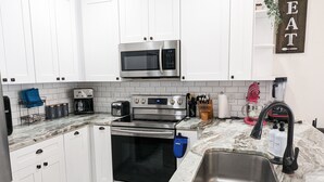 Une cuisine moderne avec des meubles blancs, des appareils en acier inoxydable, un plan de travail en marbre et un évier.