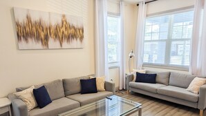 Un salon moderne avec deux canapés, une table basse en verre et un grand tableau abstrait accroché au mur.