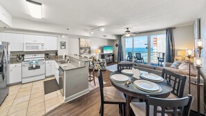 Une cuisine moderne dotée d’un îlot central, d’un coin repas avec une table ronde et des chaises, et d’un balcon offrant une vue sur l’océan.