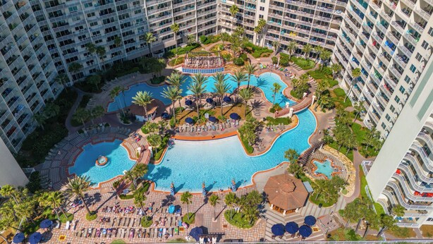 Un grand complexe hôtelier doté de plusieurs piscines, de palmiers et de chaises longues.