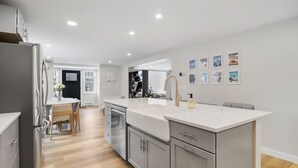 Una cucina moderna con mobili grigi, un piano di lavoro bianco e un forno integrato. C'è una zona pranzo con tavolo e sedie, e un corridoio che porta a un'altra stanza.