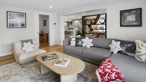 Un soggiorno moderno con un divano grigio, una poltrona beige e un tavolino in legno. Alle pareti sono presenti due opere d'arte incorniciate e una libreria con oggetti decorativi.