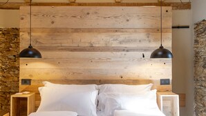 A bedroom with a wooden ceiling, a stone wall, and a bed with white linens.