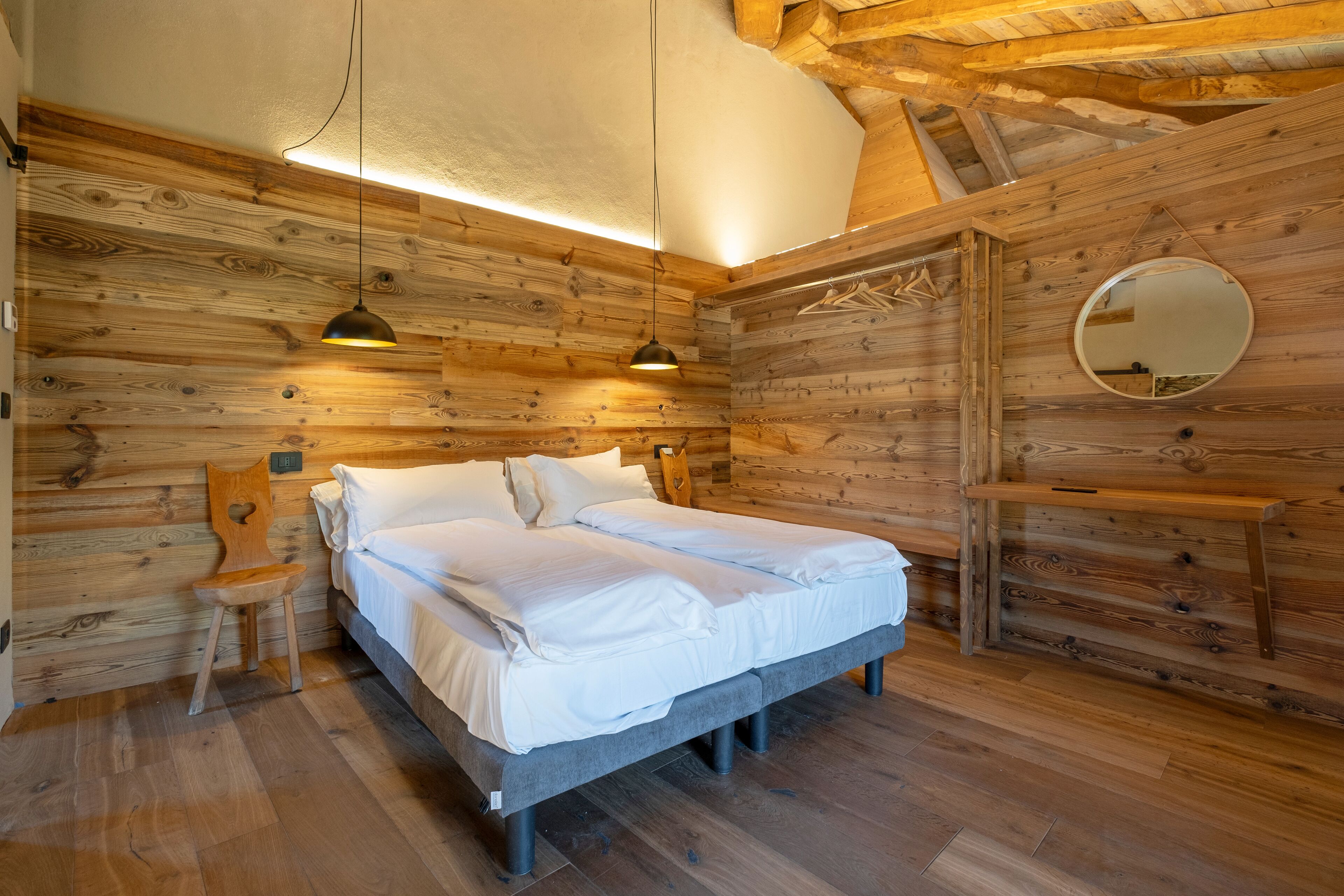 Une chambre de style cabane en bois, avec un lit, une chaise, un miroir et un luminaire suspendu.