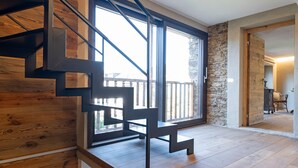 A modern staircase with wooden steps and metal railings, leading to a balcony with a stone wall and a view of the outdoors.