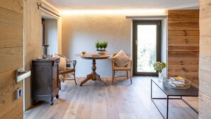 A modern interior with wooden flooring, a dining area with a table and chairs, a small cabinet, and a window with a view of greenery.