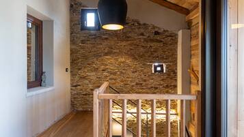Un pasillo con suelo de madera, pared de piedra, barandilla de madera y un ventanal grande.