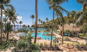A resort with a pool area surrounded by palm trees and lounge chairs.