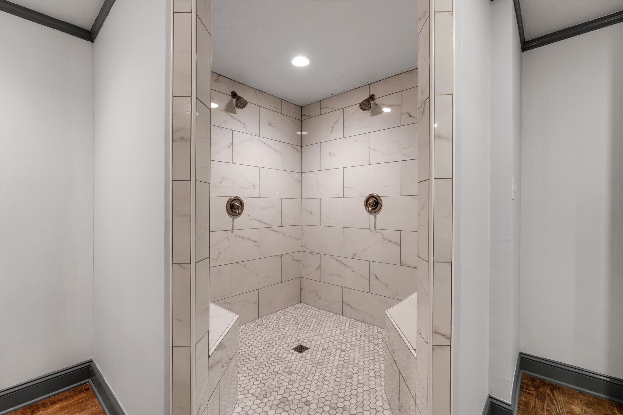 Doccia d'angolo con piastrelle di marmo bianco, pavimento a motivi esagonali e luce a incasso nel soffitto.