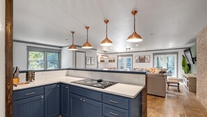 Een moderne keuken met donkerblauwe kastjes, een groot eiland en hanglampen.