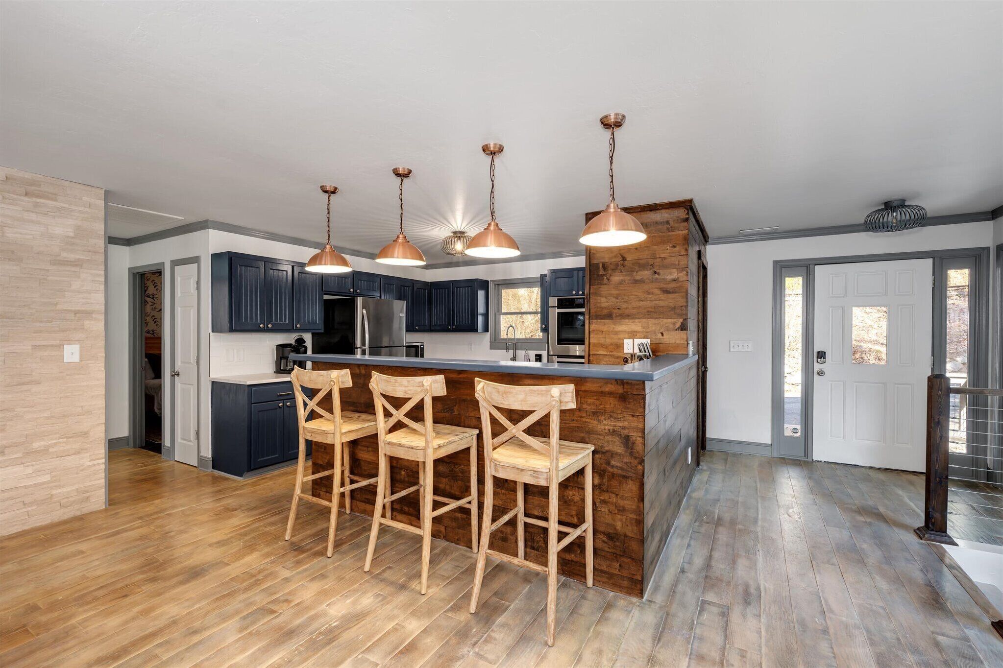 Una cocina moderna con armarios azul oscuro, una isla de madera con taburetes de bar e iluminación colgante de cobre.