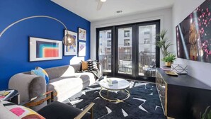 Ein modernes Wohnzimmer mit blauer Akzentwand, Deckenventilator, großem Fenster und einem schwarz-weißen Teppich.