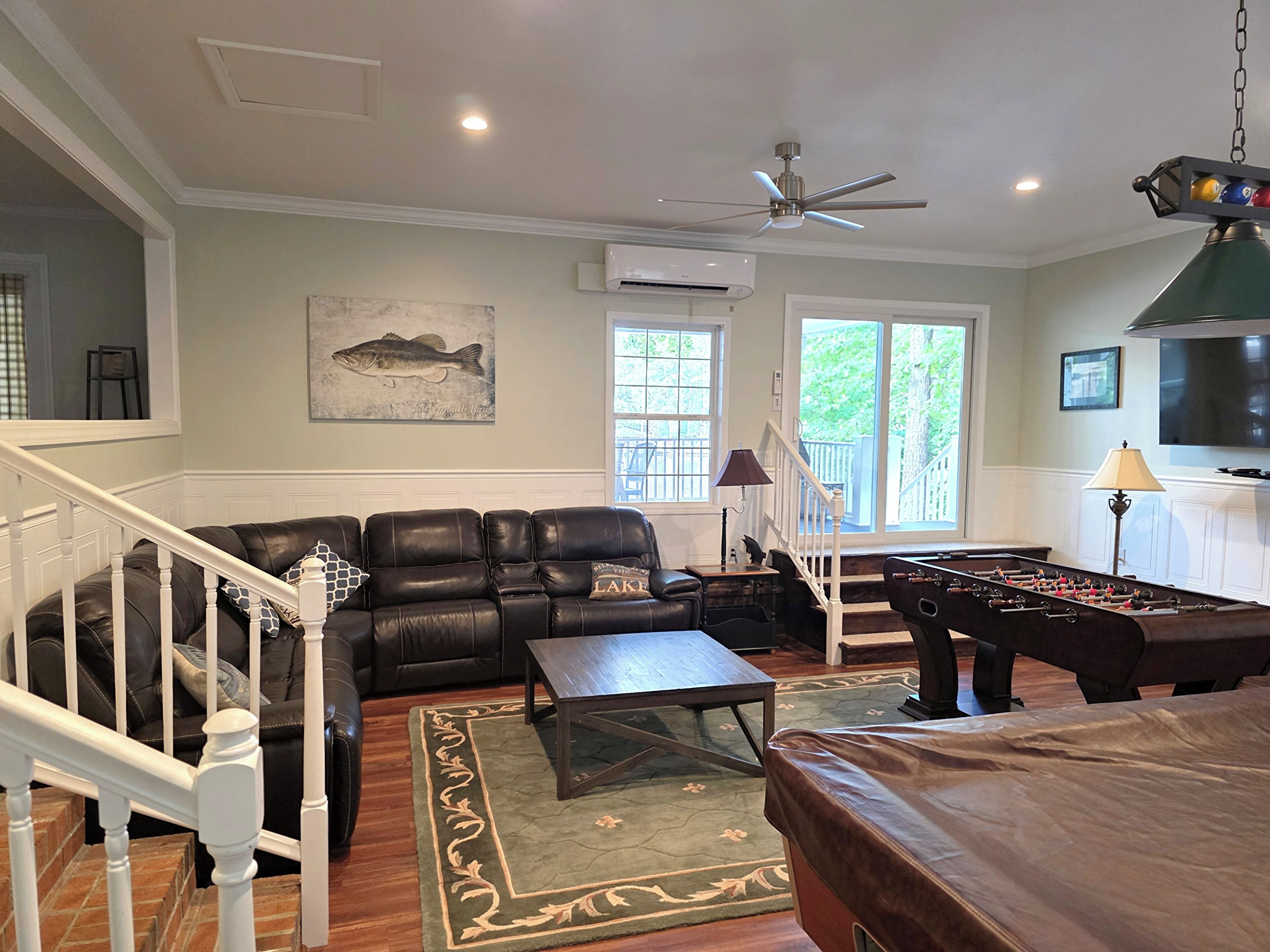 A living room with a leather sofa, a coffee table, a foosball table, a TV, and a ceiling fan.