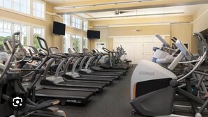 Une salle de sport avec plusieurs tapis de course alignés en rangées, de grandes fenêtres et un téléviseur à écran plat fixé au mur.