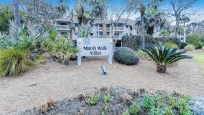 Une enseigne indiquant « Marsh Walk Villas », avec en arrière-plan un bâtiment entouré de différentes plantes et arbres.
